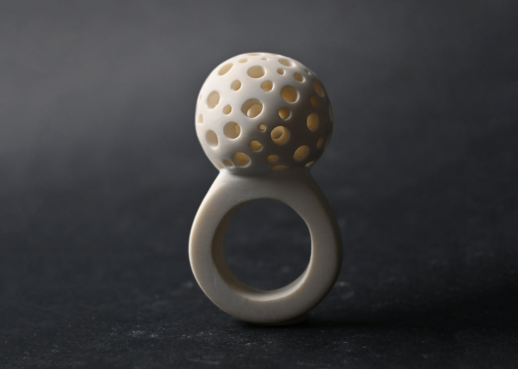 Anillo artesanal de arcilla polimérica en color blanco y adorno redondo y hueco con agujeros por los que pasa la luz de forma delicada. Diseño elegante y contemporáneo. Imagen-1