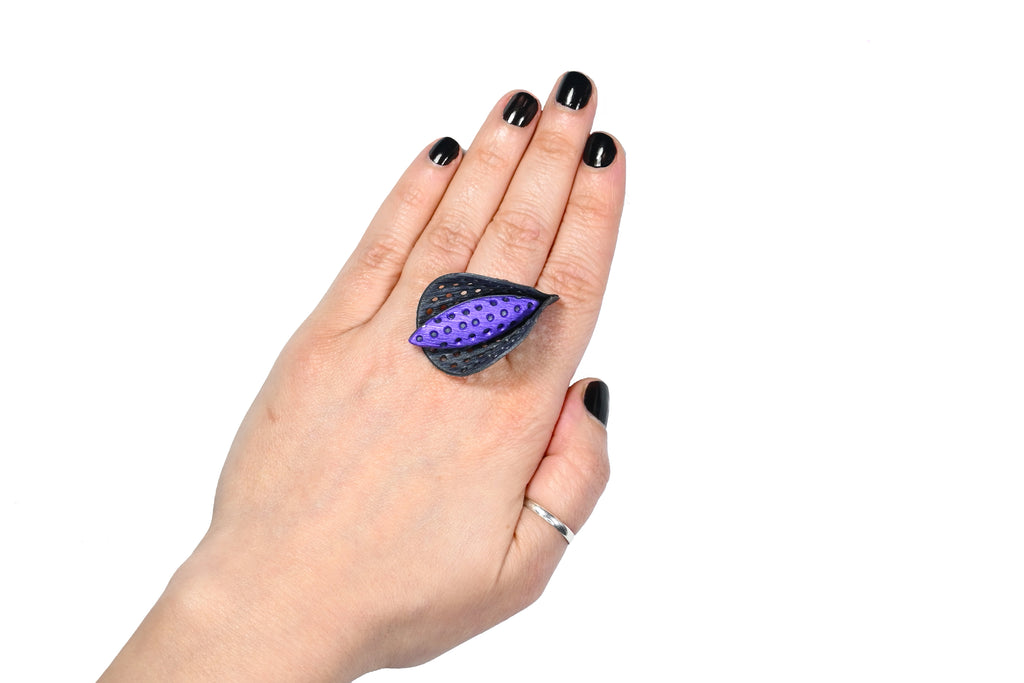 Mano luciendo el anillo artesanal de arcilla polimérica modelo Cala, en color púrpura.
