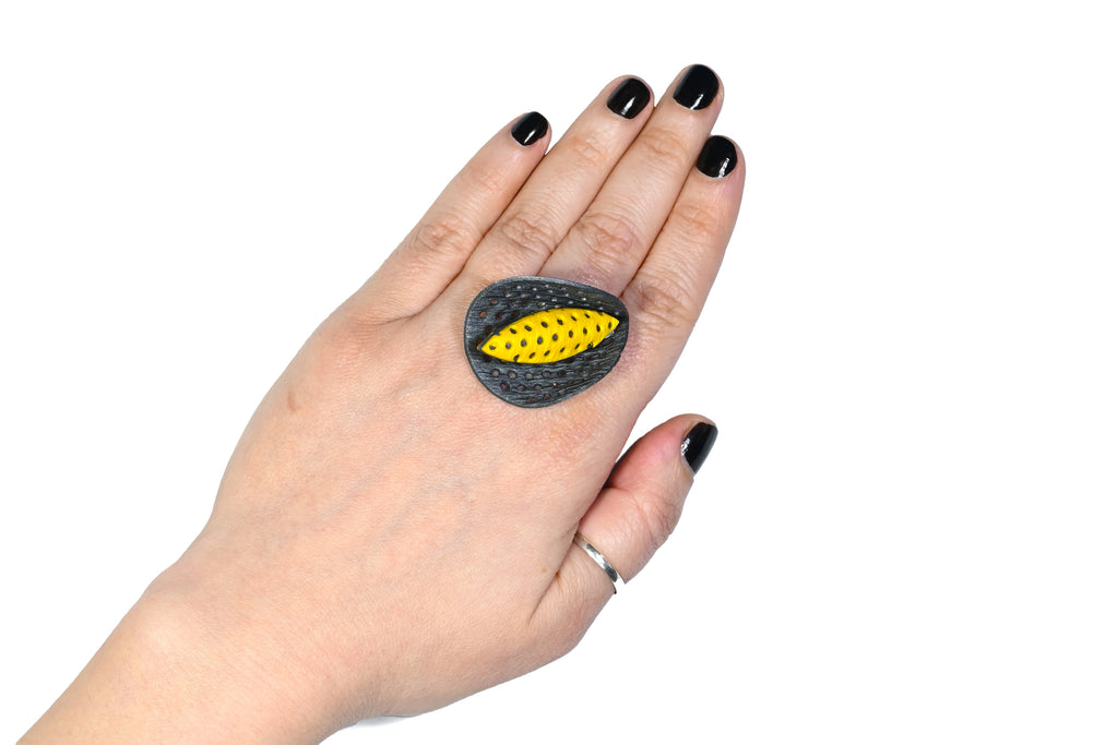 Mano luciendo el anillo artesanal de arcilla polimérica modelo Cala, en color amarillo.