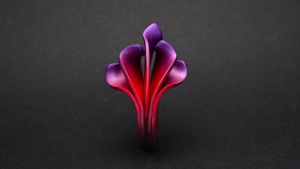 Anillo artesanal de arcilla polimérica con diseño en forma de llamas en colores metálicos, degradados de rojo a violeta.