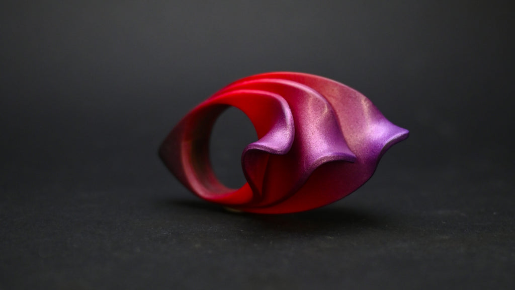 Anillo artesanal de arcilla polimérica con diseño en forma de llamas en colores metálicos, degradados de rojo a violeta.