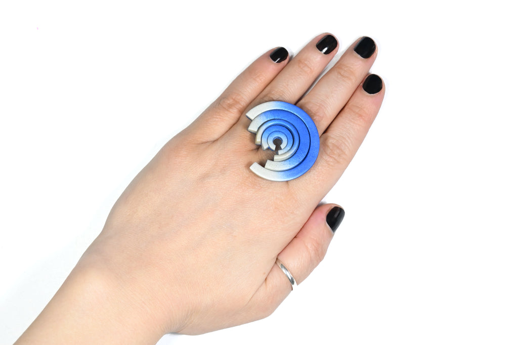 Mano con anillo artesanal de arcilla polimérica en con degradado de azul a blanco. Adorno en forma circular con distintas alturas.