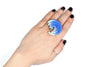 Mano con anillo artesanal de arcilla polimérica en con degradado de azul a blanco. Adorno en forma circular con distintas alturas.