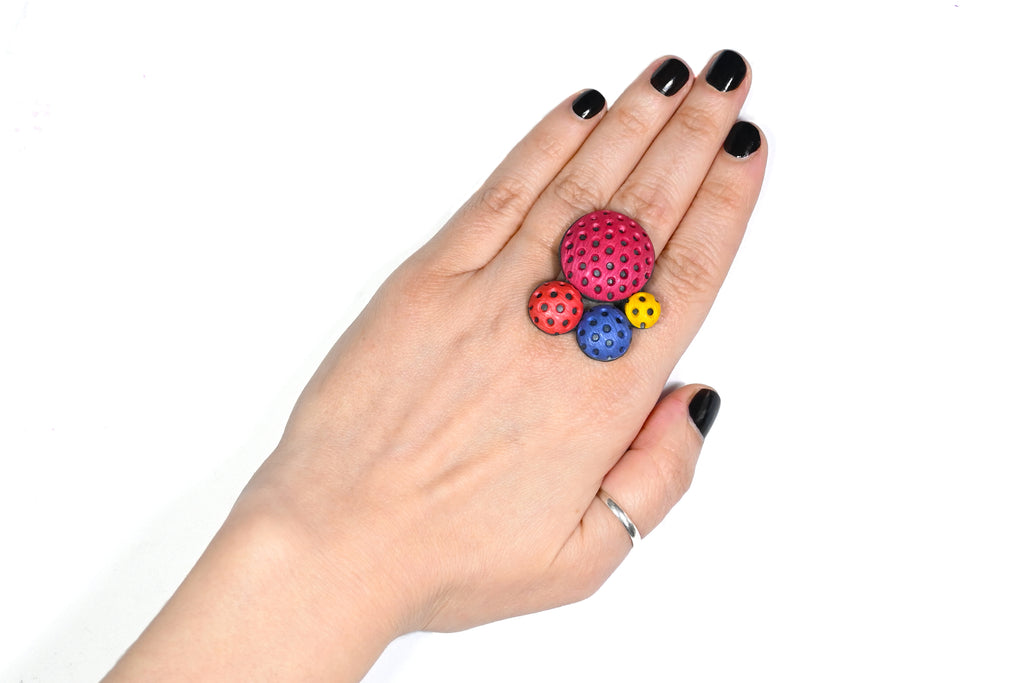 Mano luciendo el anillo artesanal de arcilla polimérica modelo Polka Dots, en color magenta.