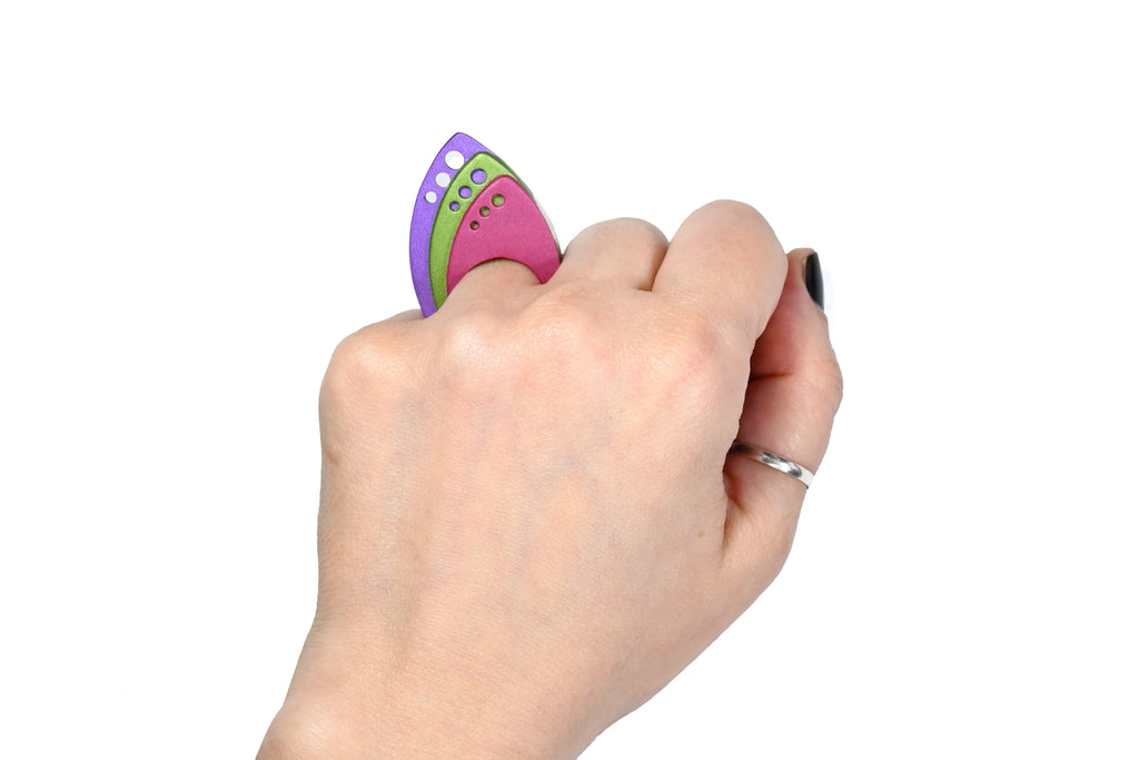 Mano luciendo el anillo artesanal de arcilla polimérica modelo Tríada, en colores granate, verde y púrpura.