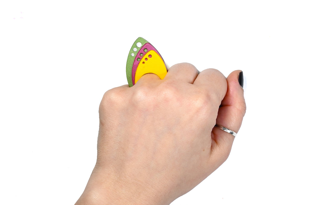 Mano luciendo el anillo artesanal de arcilla polimérica modelo Tríada, en colores amarillo, granate y verde.