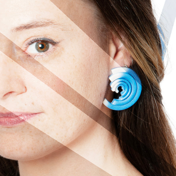 Chica luce los pendientes de arcilla polimérica Mistral, con diseño de segmentos de círculos concéntricos y degradado de color de blanco a azul cielo.