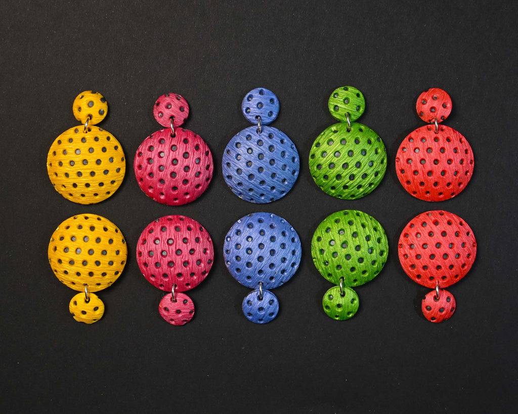 Imagen de los pendientes hechos a mano, modelo Polka Dots en cinco colores sobre fondo negro, colocados en forma rectangular 