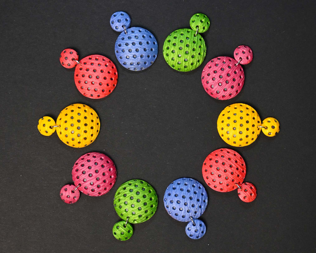 Imagen de los pendientes hechos a mano, modelo Polka Dots en cinco colores sobre fondo negro, colocados en forma circular 