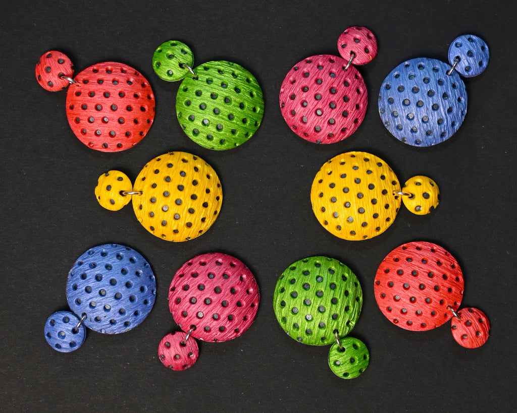 Imagen de los pendientes hechos a mano, modelo Polka Dots en cinco colores sobre fondo negro, colocados en forma original 