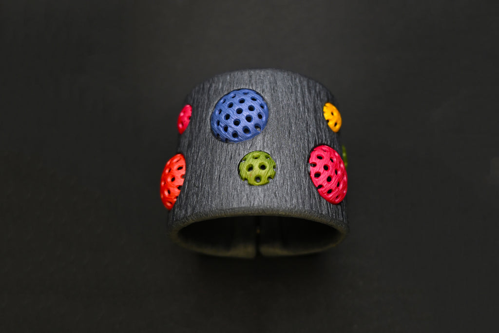 Detalle de la pulsera artesanal de arcilla polimérica, Polka Dots, de colores vibrantes, sobre fondo negro.